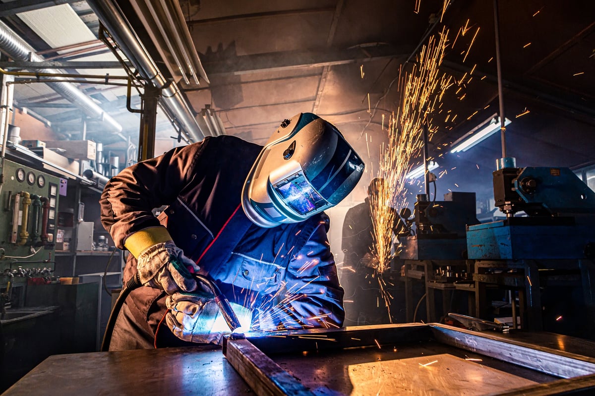 A welder joins steel plate with a welding torch, illustrating the heat-treatment and weldability behaviour that distinguishes alloy steel